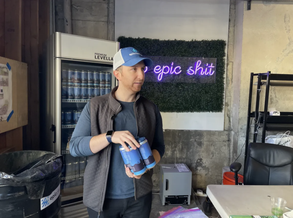 Epic CEO Aaron Tartakovsky holding four cans of Epic OneWater Brew in the Epic Soil Hub